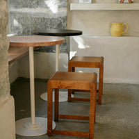 Wooden and black stools beside a round pink-top table with a white base against a textured gray background.