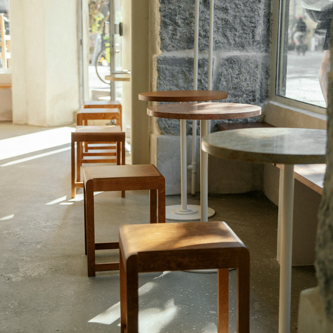 "Light wood stools and a round marble table in a bright, modern interior with sunlight streaming in."
