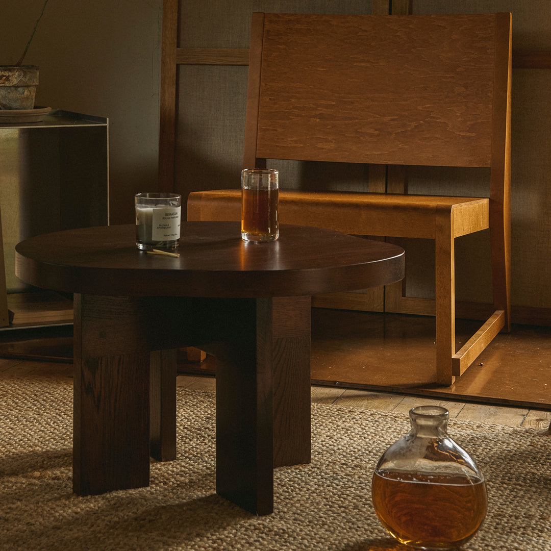 Dark wood circular coffee table with minimalist design, surrounded by neutral tones and natural textures.