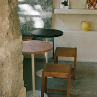 Black, pink, and natural wood accent tables with simple patterns, set against a textured stone backdrop.