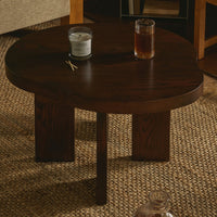 Dark brown circular coffee table with a smooth surface and minimalist wooden legs, set on a woven texture rug.