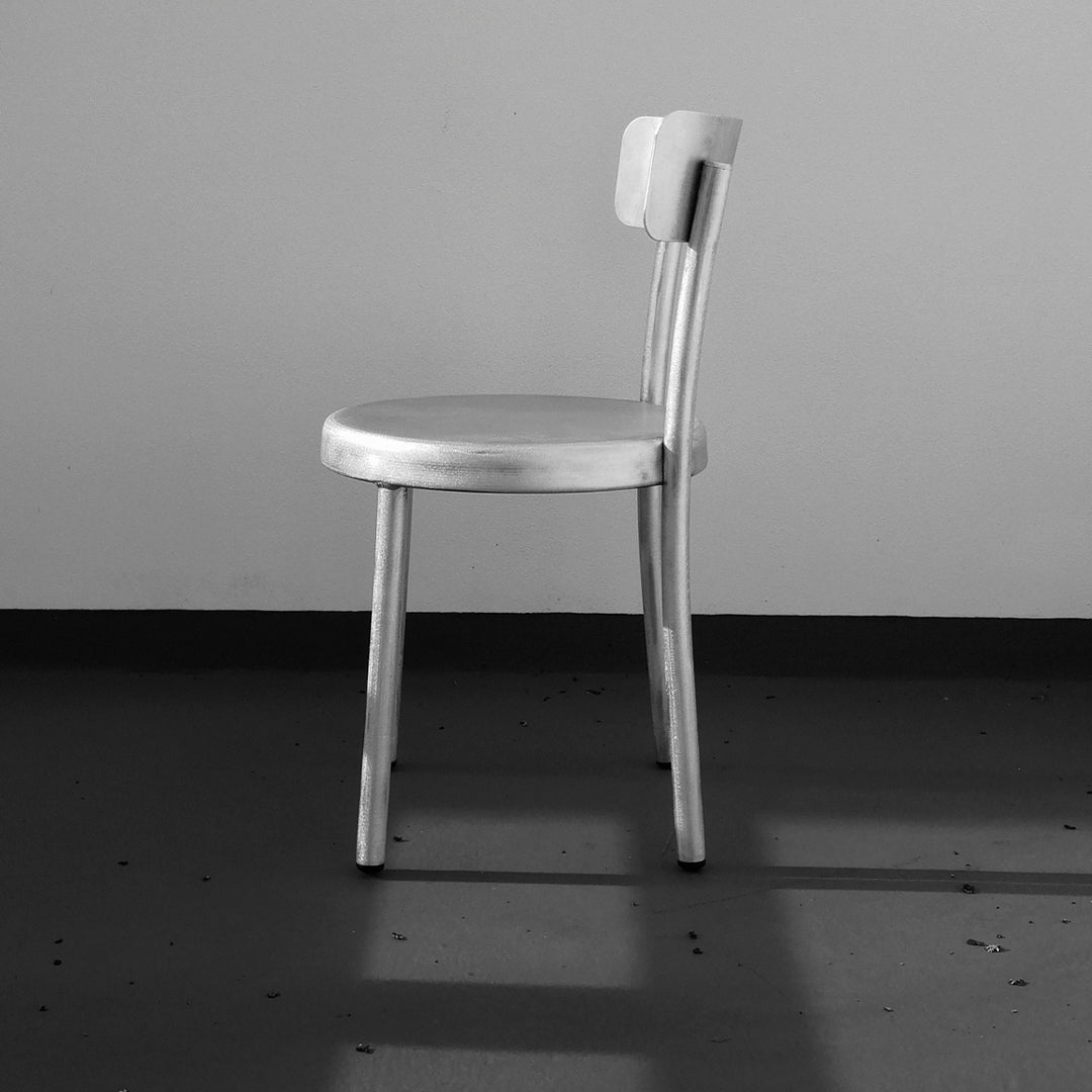 Minimalist gray chair with a sleek metallic finish and smooth, simple lines against a neutral background.