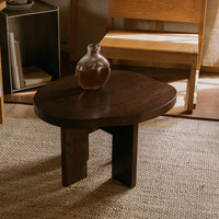 Dark wood round coffee table with smooth surface and minimalist design, complemented by natural, neutral tones in the setting.