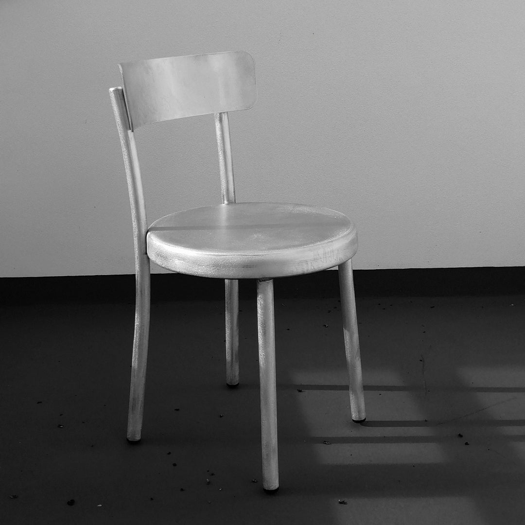 Minimalist silver chair with a smooth finish, featuring a sleek design and simple, modern lines.