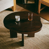 Dark wood coffee table with an organic, irregular shape, paired with a neutral rug and soft, warm lighting.
