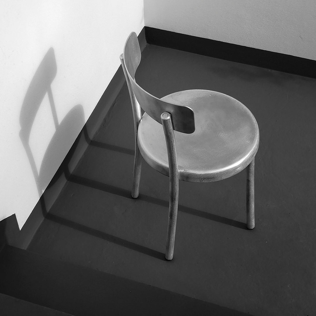 Minimalist black and white chair with sleek design, casting shadows on a dark floor.