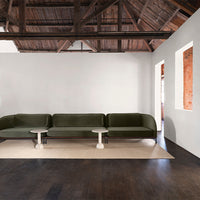 Sleek dark green velvet sofa with a light-colored round side table, complemented by a neutral rug on dark wood flooring.