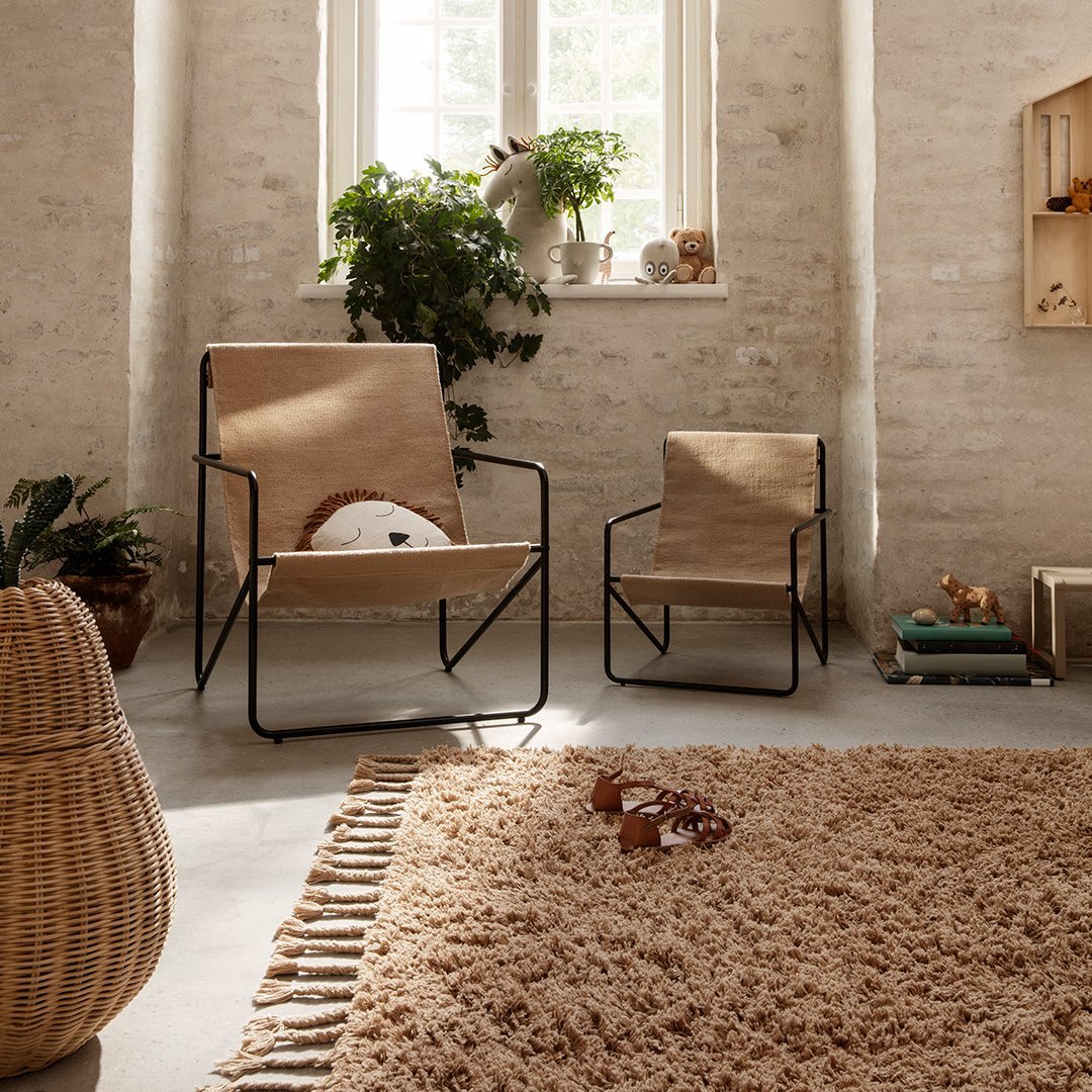 Light beige chairs with black frames, complemented by a textured, fluffy brown rug and natural greenery accents.