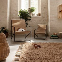 Light beige chairs with black frames, complemented by a textured, fluffy brown rug and natural greenery accents.