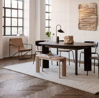 Modern dining room featuring a brown wooden table, black chairs, and a beige rug with a rustic texture.
