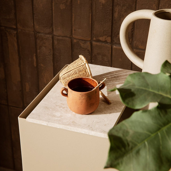Terracotta cup with natural textures, set against a minimalist beige background and green foliage.