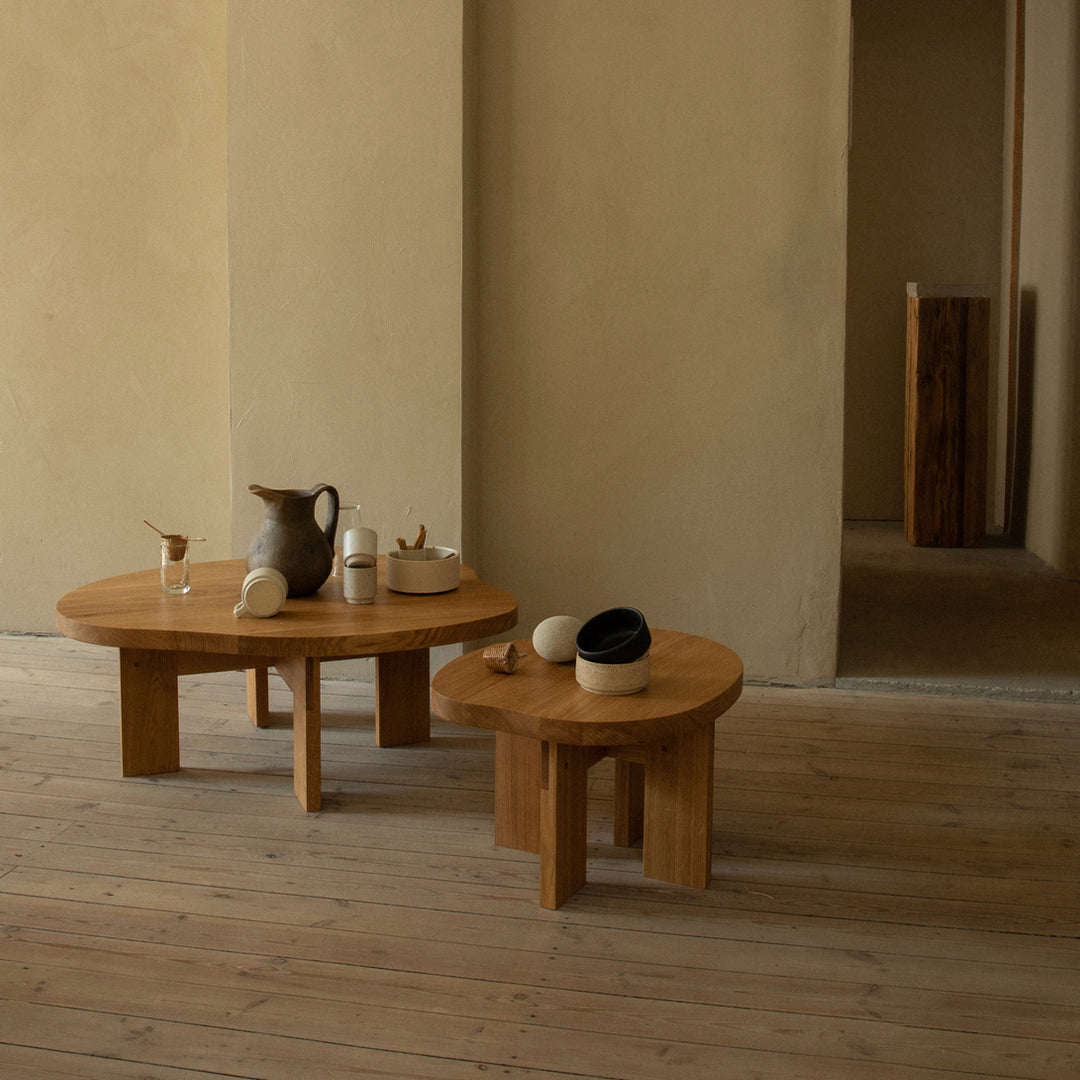 Wooden coffee tables in natural finish, featuring simple round shapes and subtle patterns, complemented by minimalistic decor.