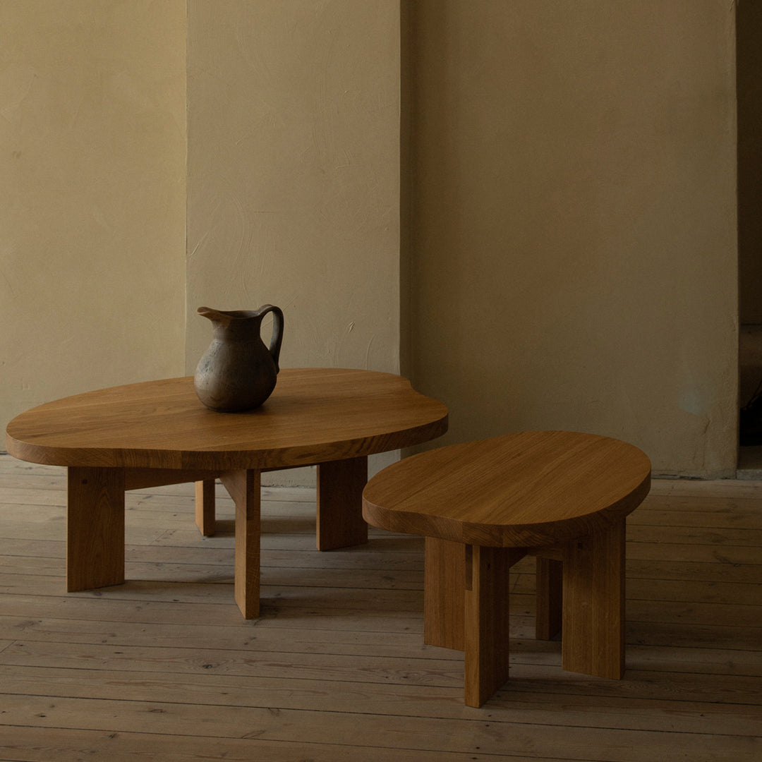 Natural wood coffee tables in warm, honey tones with smooth, oval shapes; minimalist design on a light wooden floor.