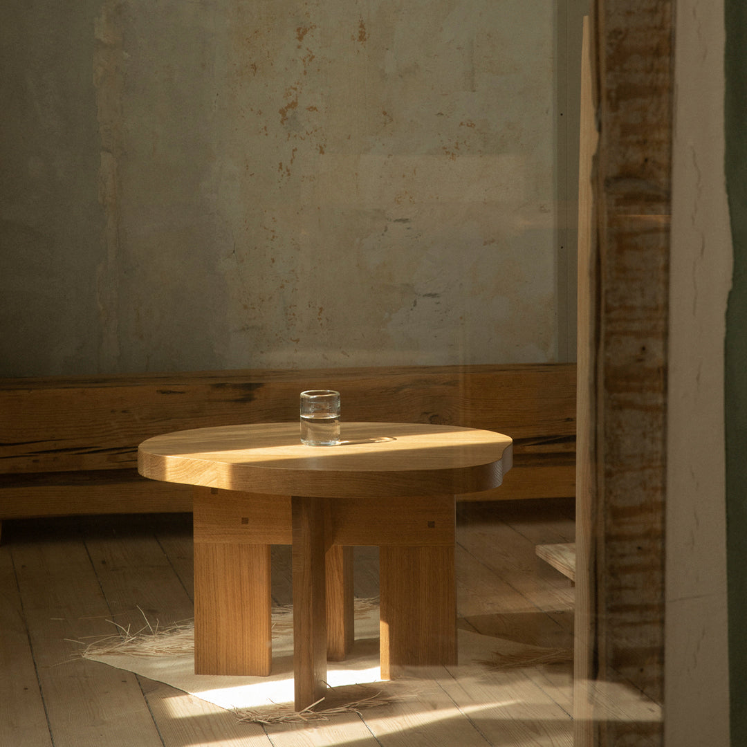 Light wood round coffee table with a natural finish, set against a muted, textured wall.