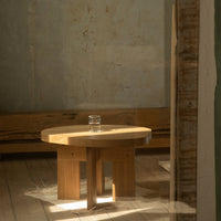 Light wood round coffee table with a natural finish, set against a muted, textured wall.