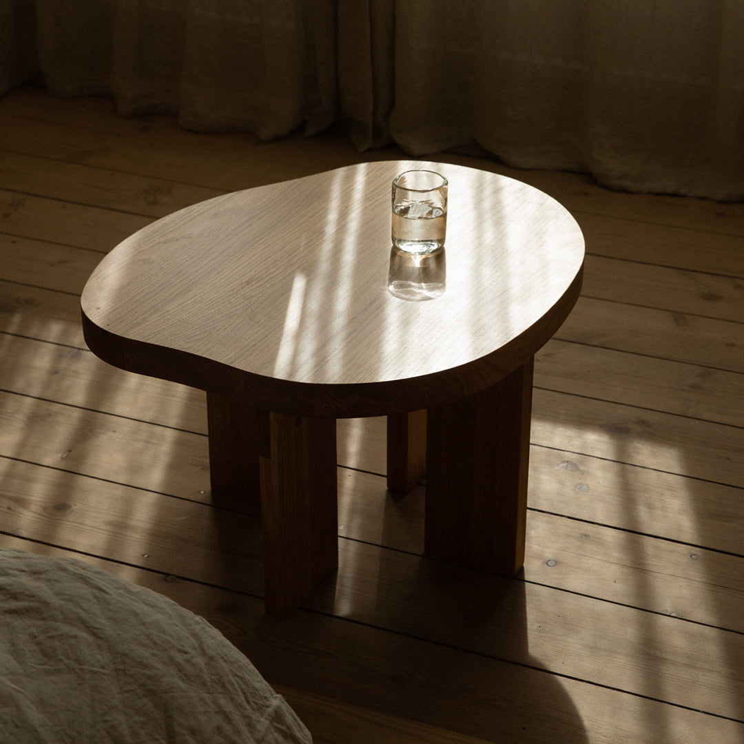 Natural wood coffee table with a smooth, organic shape and light grain pattern, illuminated by soft, ambient light.