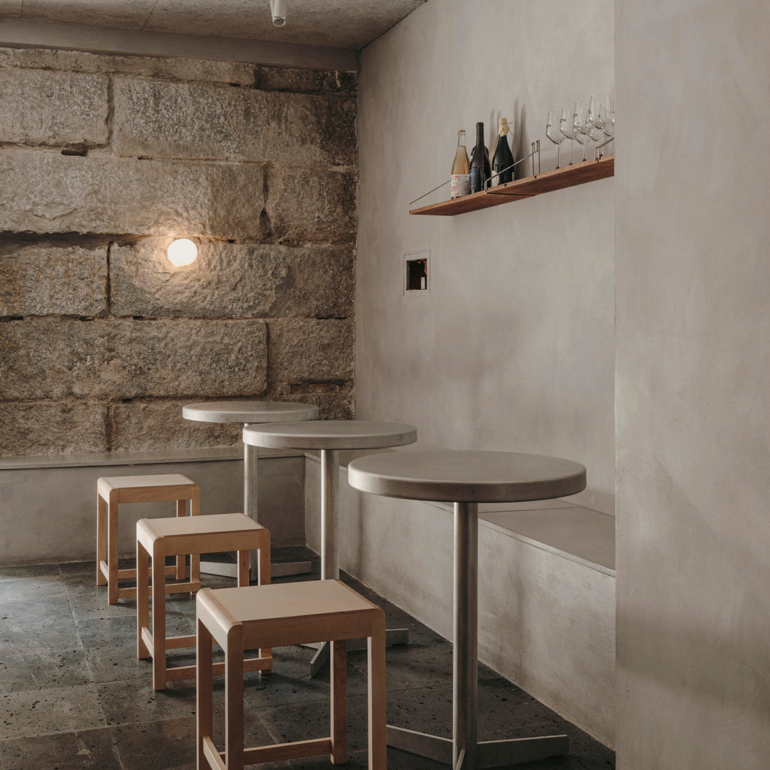 Modern minimalist bar with warm beige walls, grey stone textures, and light wooden stools. Elegant and inviting atmosphere.