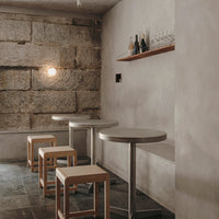 Modern minimalist bar with warm beige walls, grey stone textures, and light wooden stools. Elegant and inviting atmosphere.