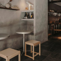 Minimalist interior featuring gray walls, sleek silver table, and light wooden stools against dark stone flooring.