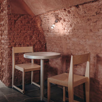 Light wood chairs and a round table against a textured pink brick wall, creating a warm, cozy atmosphere.