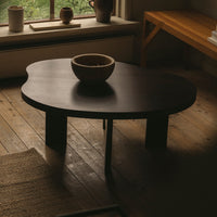 Dark wood coffee table with a unique organic shape and sleek black finish, complemented by a round ceramic bowl on top.