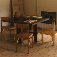 Wooden dining table with natural finish, paired with light wood chairs, set against a neutral-toned room.