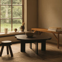 "Natural wood grains in warm tones; round black table, light wood bench, and rustic decor in a cozy setting."