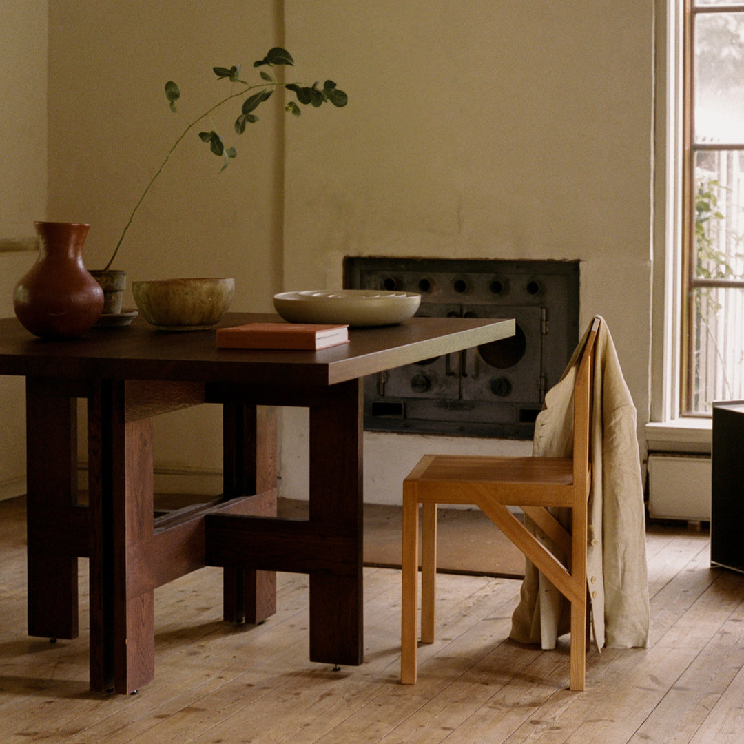 "Modern wooden table in deep brown with minimalist cream chair and soft green accents from plants and decor."