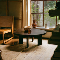"Round black coffee table with a smooth finish, set against warm wooden tones and natural light accents."