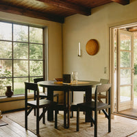 Black wooden dining table with beige chairs, light neutral walls, and natural textures from woven decor and rugs.