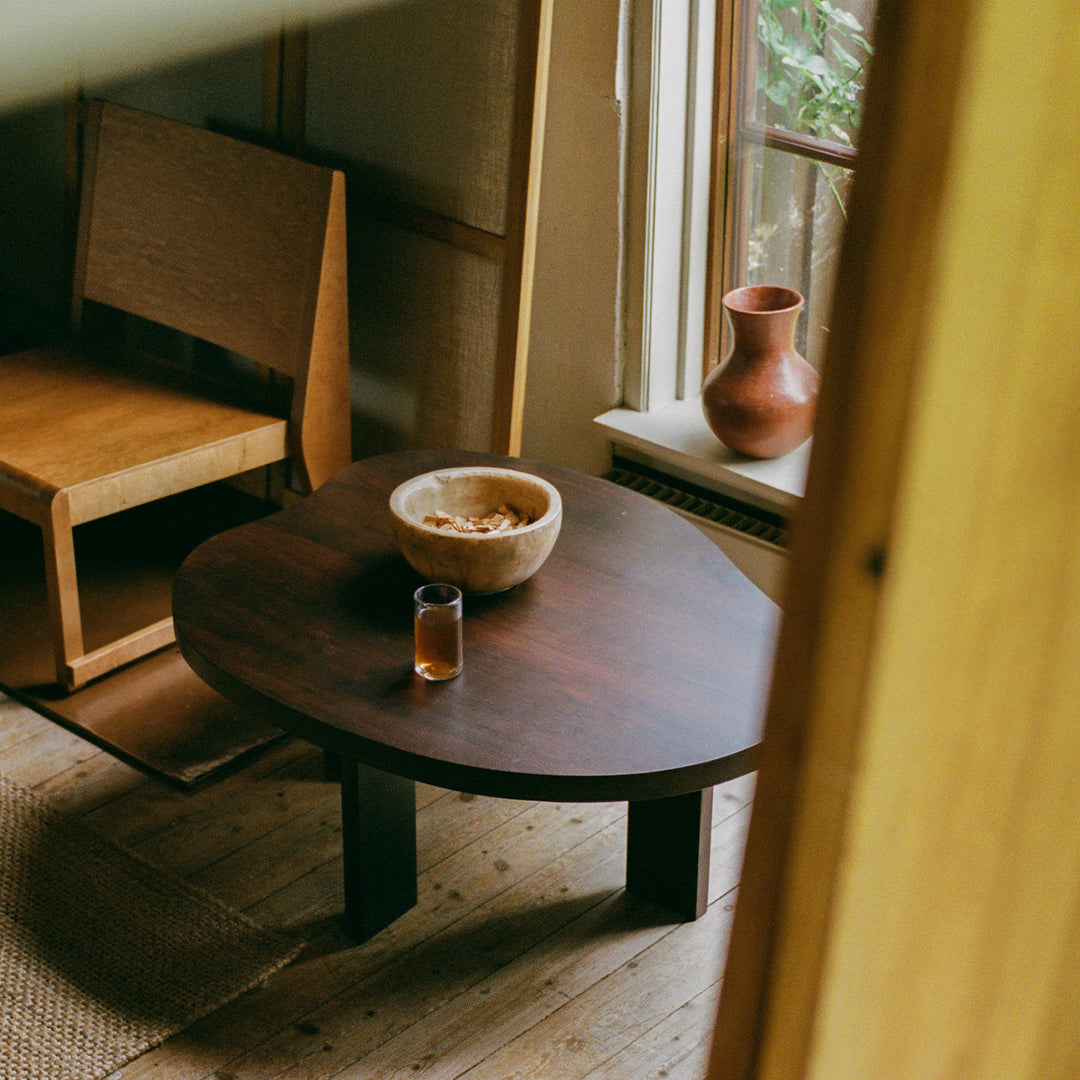 Dark wooden round coffee table with a smooth finish, surrounded by natural tones and organic textures.