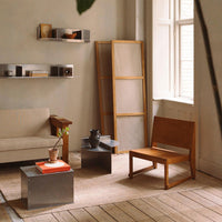 Minimalist living room featuring beige sofa, wooden chair, and gray metal tables with a neutral rug.