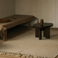 Brown textile drapes over a light tan rug, accented by a dark wooden table and a simple ceramic vase.