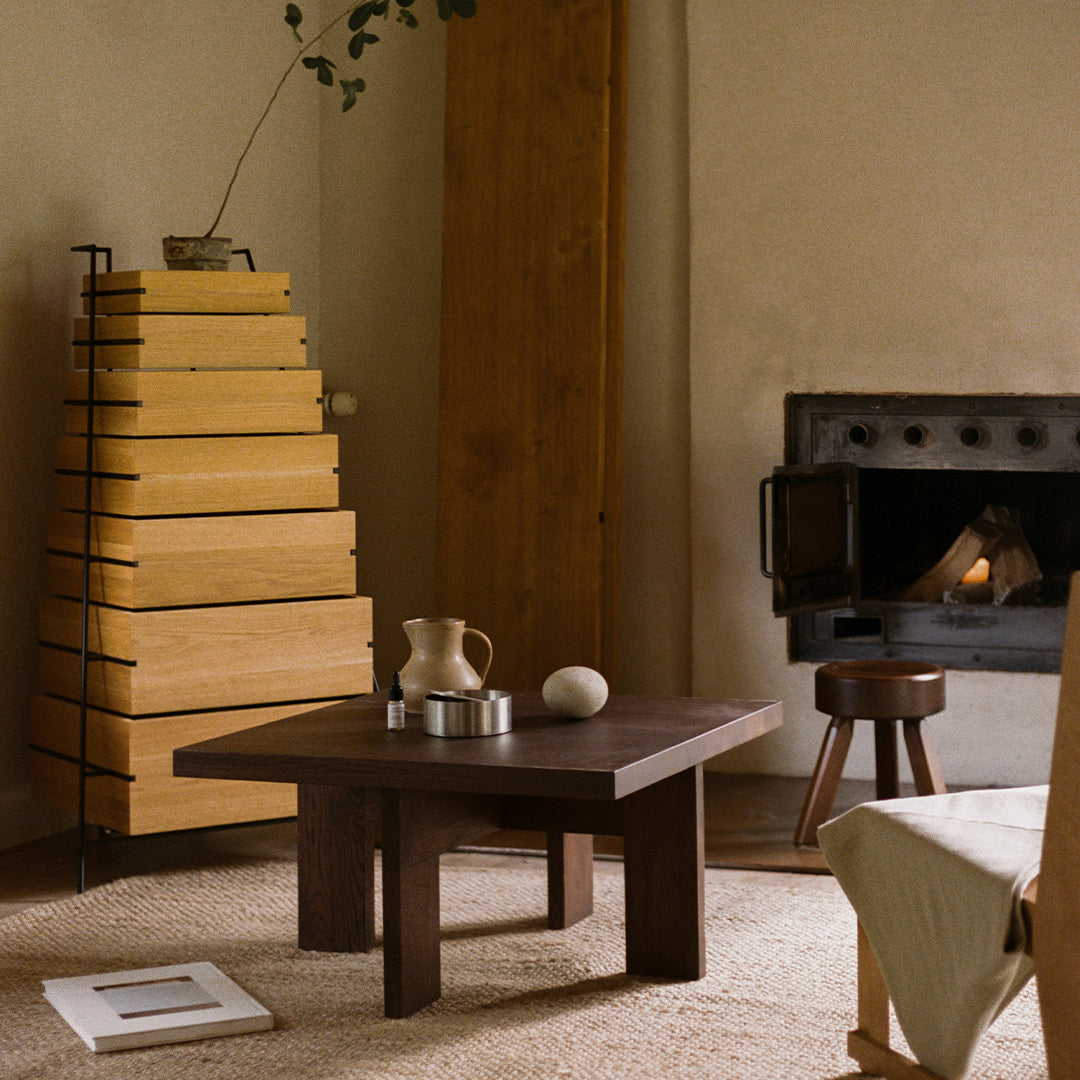 Dark wood coffee table with natural wood accents and earthy tones in a cozy room setting. Soft textiles add warmth.