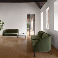 Green velvet sofas with curved designs, set against a light wooden floor and white walls.