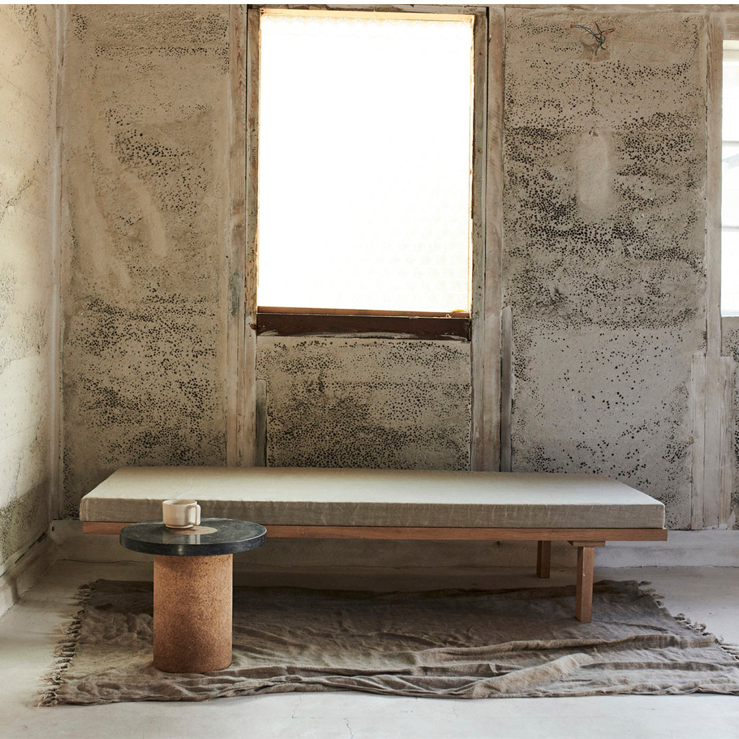 Neutral-toned minimalist sofa with a smooth surface and natural wood accents, set against a textured gray wall.