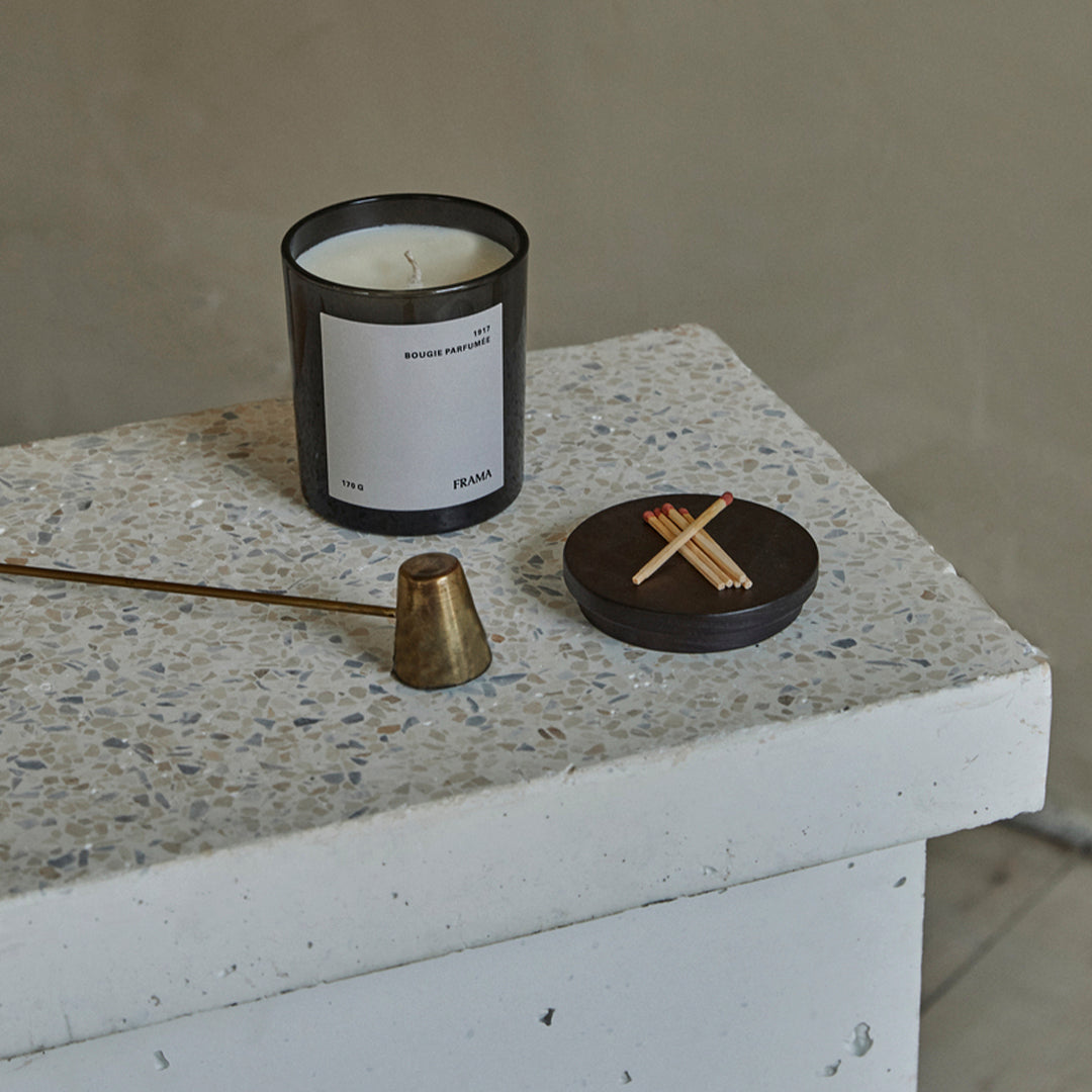 Black and white candle on textured light gray surface with bronze accent and circular dark container.