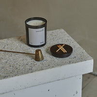 Black and white candle on textured light gray surface with bronze accent and circular dark container.
