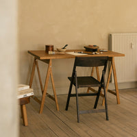 Natural wood tones with a black folding chair against a warm beige backdrop and light wooden flooring.