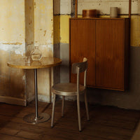 Wooden table with a round top, silver chair, and rustic yellow and gray wall accents create a warm, minimalist vibe.