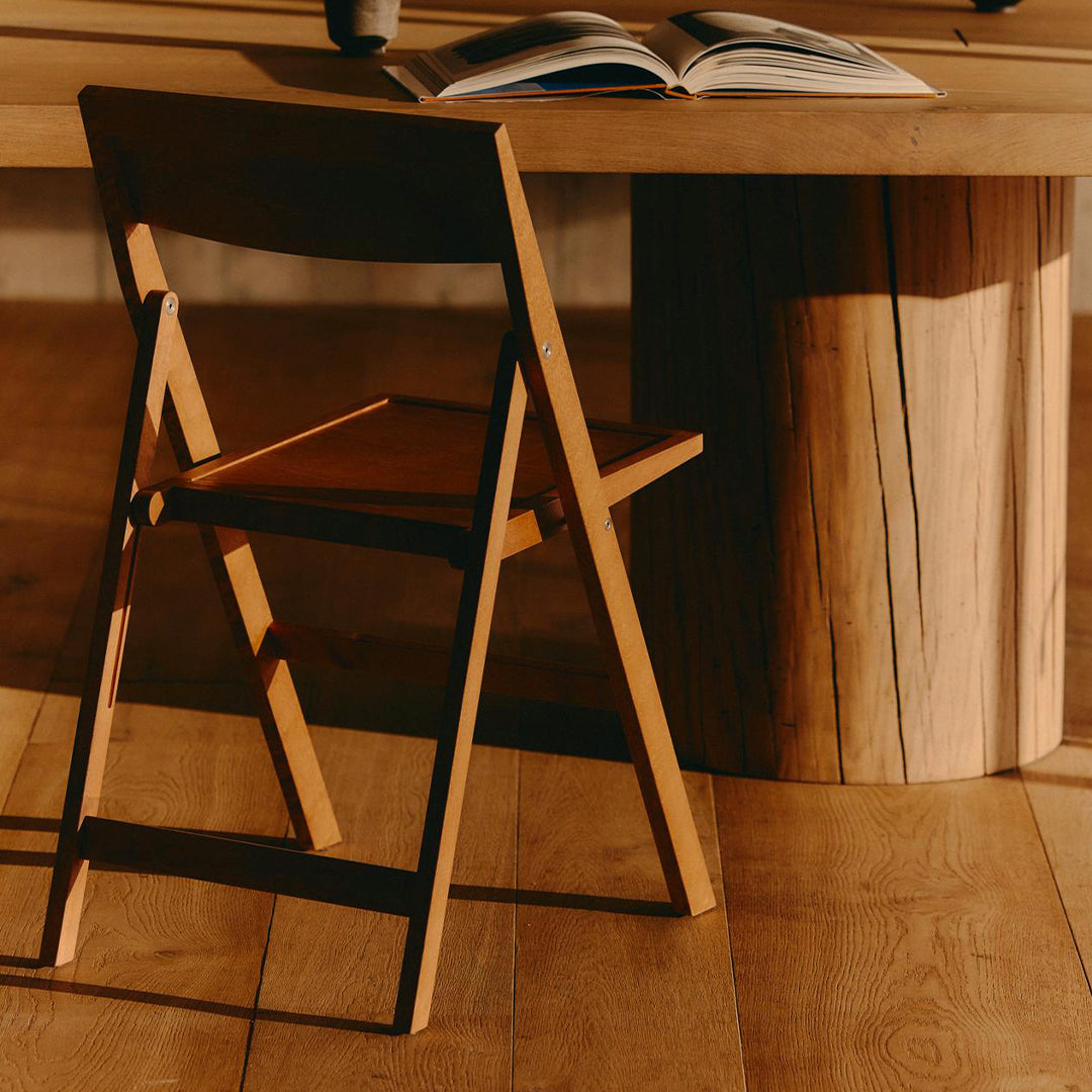 Wooden folding chair with natural finish, featuring warm tones and a simple design against a textured wood table.
