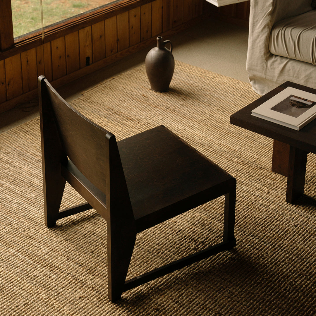Black wooden chair with a minimalist design, set on a textured tan woven rug, creating a modern, earthy aesthetic.