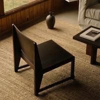 Black wooden chair with a minimalist design, set on a textured tan woven rug, creating a modern, earthy aesthetic.