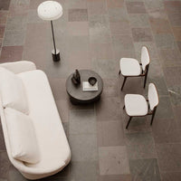 Cream sofa and white chairs on a textured gray stone floor, accentuated by a minimalist black table and lamp.
