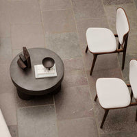Modern round coffee table with a silky gray finish, surrounded by minimalist white chairs and soft earth-toned floor tiles.