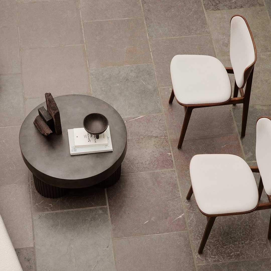 Modern round coffee table with a silky gray finish, surrounded by minimalist white chairs and soft earth-toned floor tiles.