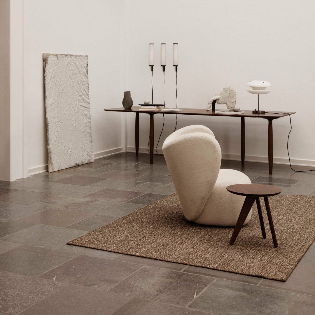 Beige curved chair on a textured brown rug, surrounded by neutral-toned decor and gray stone flooring.
