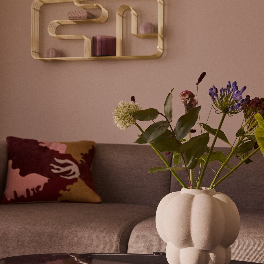 "Neutral-toned vase with textured design, vibrant floral arrangement, and colorful abstract pillow in a cozy living space."
