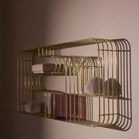 Gold wire shelf with soft pink containers and a floral-patterned box, casting elegant shadows on a wall.
