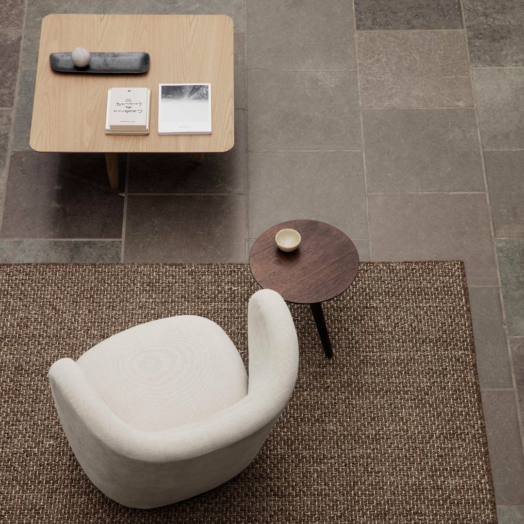 Cozy cream chair on textured brown rug, paired with a wooden coffee table and minimalist decor in neutral tones.